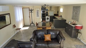 A living room with a black leather sofa, a dining table, and a kitchen in the background. - La Magnanerie de L'estrade (rosières)