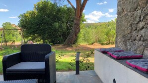 A patio with a wicker chair and a bench, a stone wall, and a row of cushions. - La Magnanerie de L'estrade (rosières)