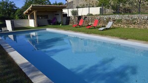 A rectangular swimming pool with a stone wall and a covered patio area. - La Magnanerie de L'estrade (rosières)