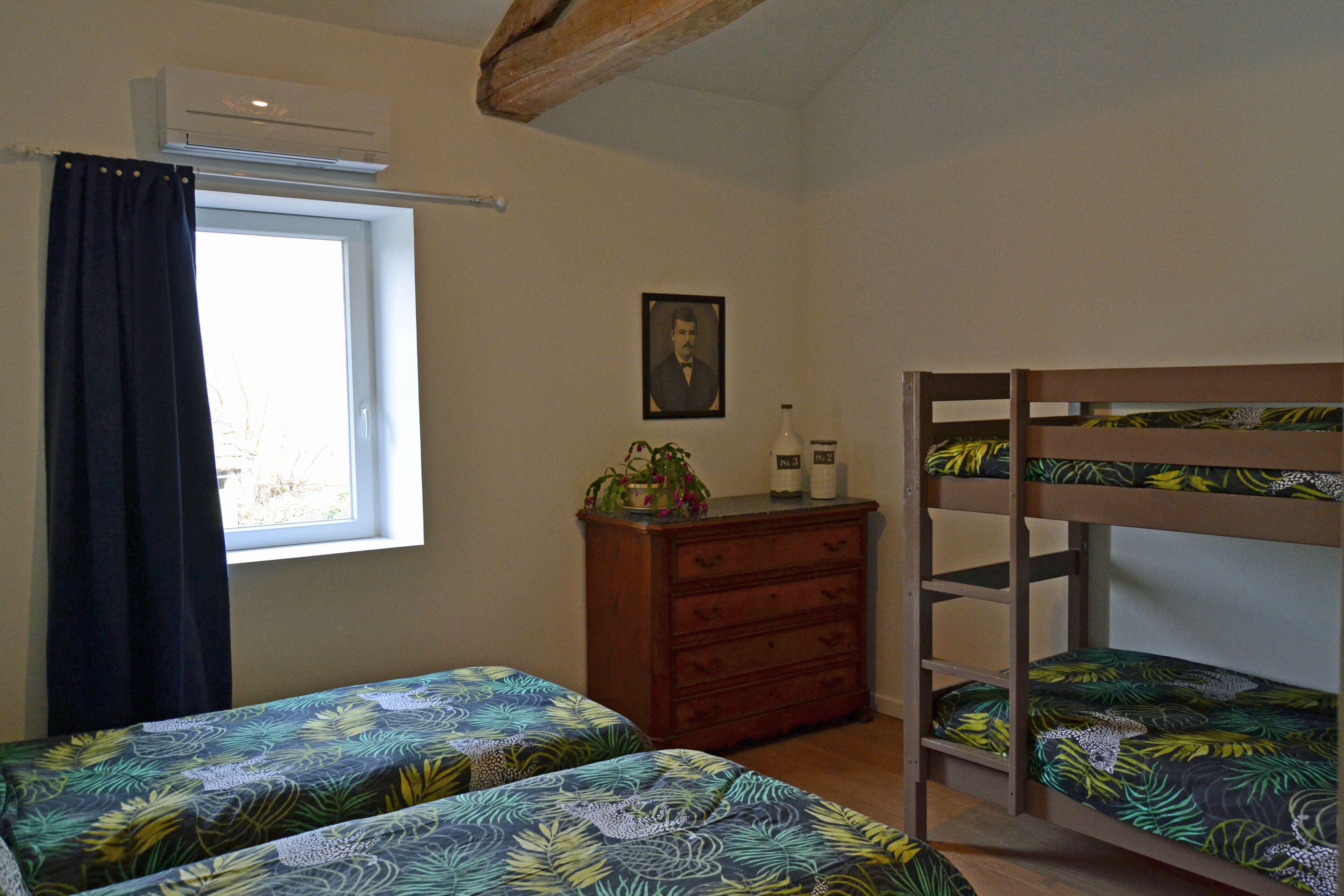 A bedroom with two bunk beds, a dresser, a window with a curtain, and a framed picture on the wall.