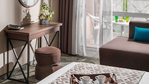 A hotel room with a bed, a desk with a mirror, a small round table with a tray of cups and a book, a window with a view of the sea, and a balcony with a table and chairs. - Alba (Nessebar)