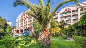 A hotel with a central courtyard featuring a palm tree, surrounded by lush greenery and a swimming pool. - Alba (Nessebar)