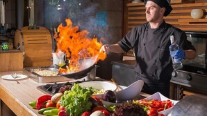 A chef cooking with a large flame, surrounded by fresh vegetables and cooking utensils. - Alba (Nessebar)