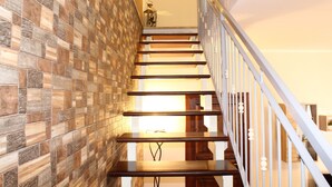 Un escalier avec des marches en bois et des rampes blanches, menant à un palier dont un mur est recouvert de carreaux.