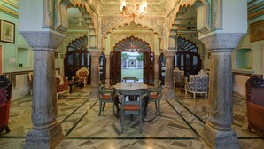 A grand hall with ornate arches, a chandelier, and a central table with chairs. - Hotel Rajmahal Palace (Devli)