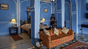 A room with blue walls, a striped sofa, a bed, and a small table with a lamp. - Hotel Rajmahal Palace (Devli)