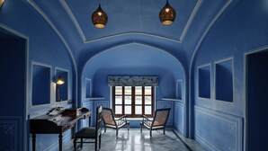 A room with blue walls, a marble floor, a desk, two chairs, and a window with a view. - Hotel Rajmahal Palace (Devli)