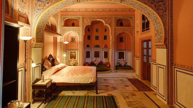A traditional room with an ornate archway, a bed with pillows, a nightstand, and a lamp. - Hotel Rajmahal Palace (Devli)
