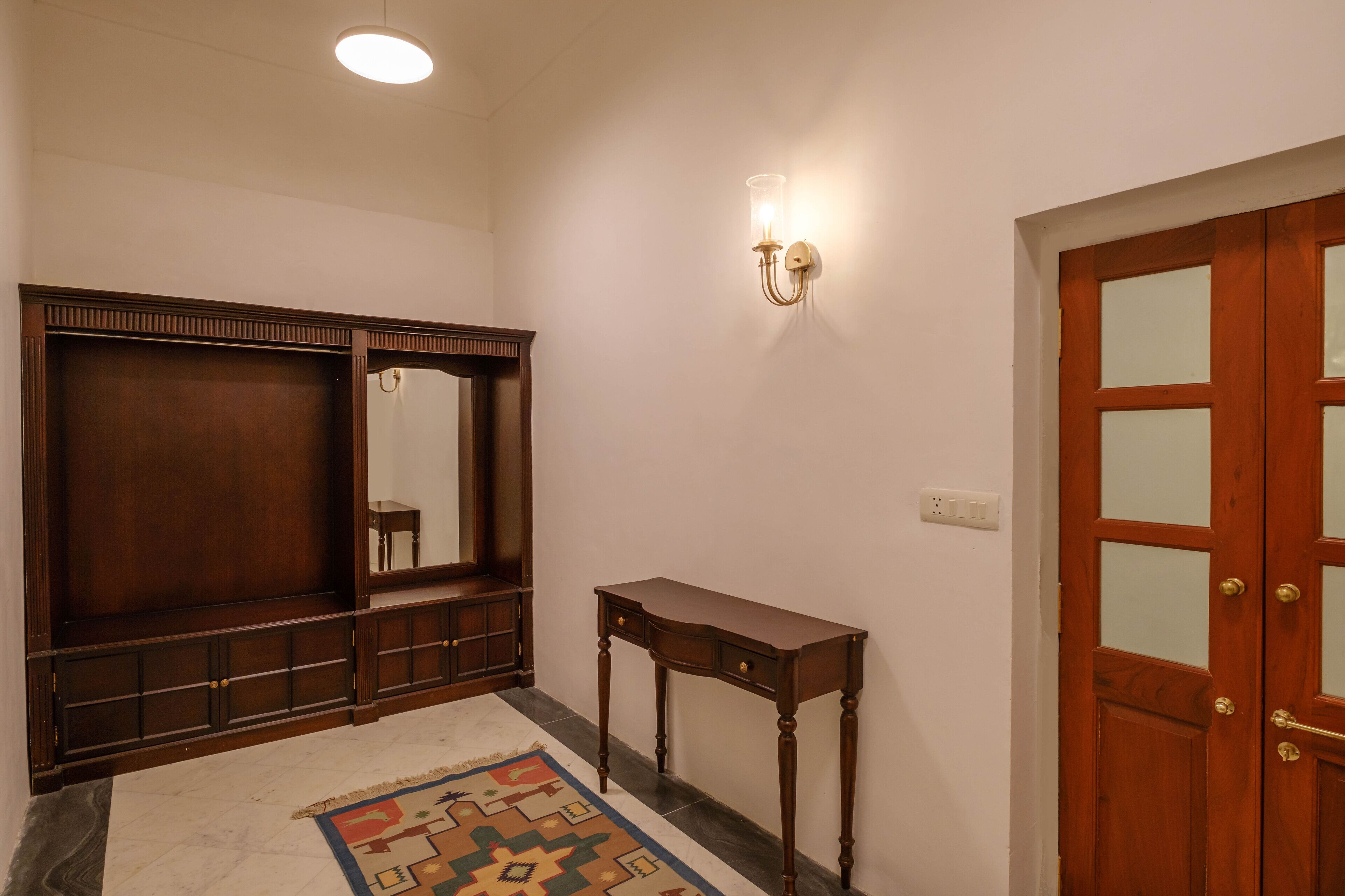 A room with a wooden wardrobe, a small table, a mirror, and a door with glass panels.