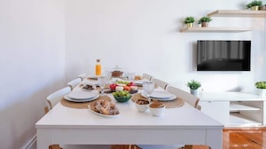 Un comedor moderno con una mesa blanca dispuesta para una comida, rodeada de sillas.