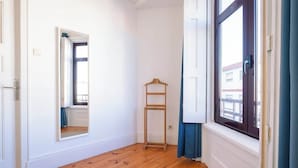 Una habitación con piso de madera, un espejo, una escalera de madera y una ventana con cortinas.