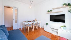 Una sala de estar moderna con comedor, suelo de madera, televisor de pantalla plana y estanterías empotradas con plantas.