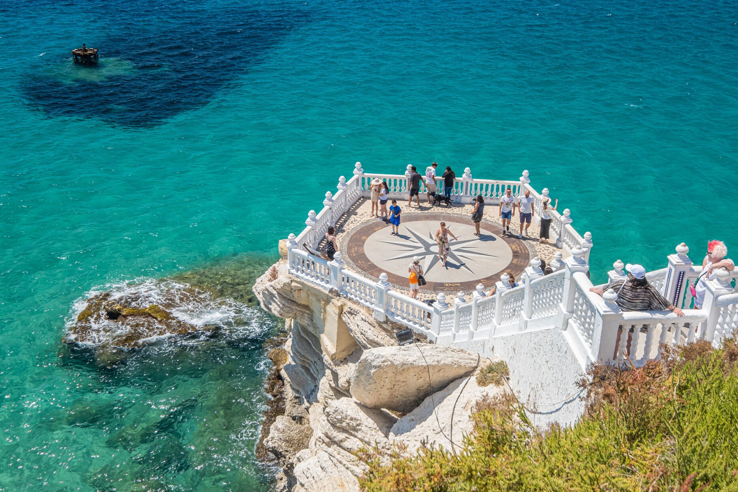 A coastal viewpoint with a circular viewing platform, white railings, and clear turquoise waters.