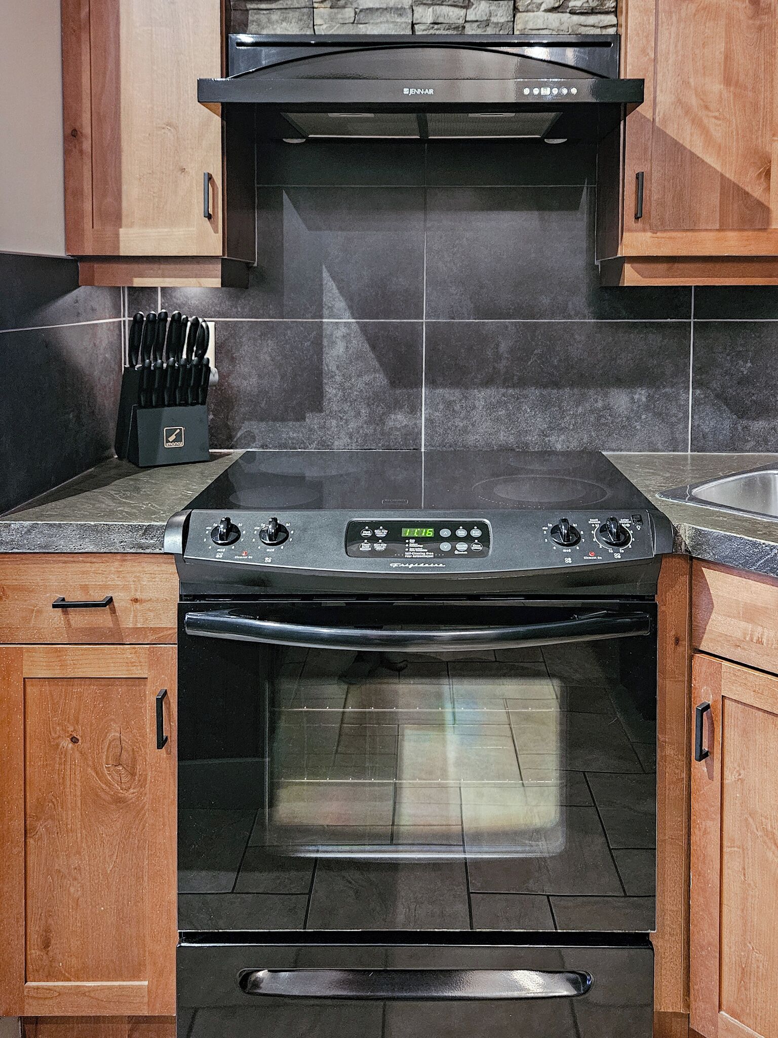 A kitchen with a black stove, wooden cabinets, and a knife block.