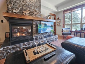 Una sala de estar acogedora con chimenea de piedra, un televisor de pantalla plana y una zona de estar cómoda con vistas al exterior.