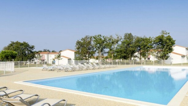 Une piscine avec des chaises longues et un ciel dégagé.