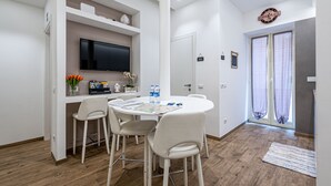 A modern kitchen with white cabinetry, a flat-screen TV, and a dining area with a round table and white chairs.