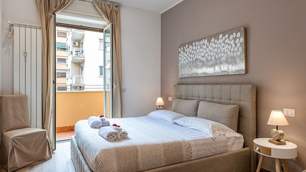 A hotel room with a large bed, a chair, a bedside table with a lamp, and a view of the outside balcony.