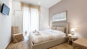 A modern bedroom with a large bed, a bedside table with a lamp, a chair, and a television mounted on the wall.