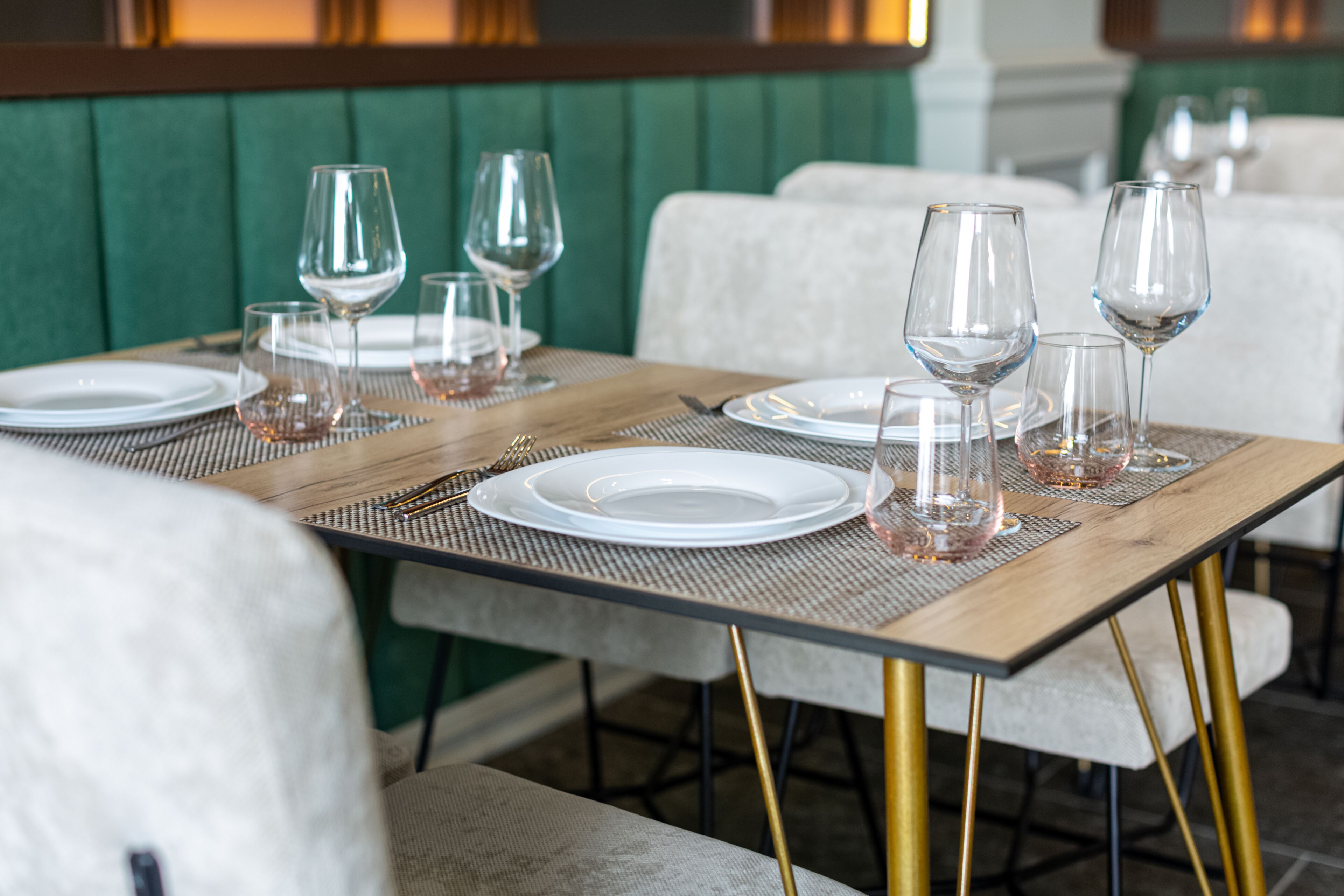 A dining table set with plates, glasses, and cutlery, surrounded by upholstered chairs.
