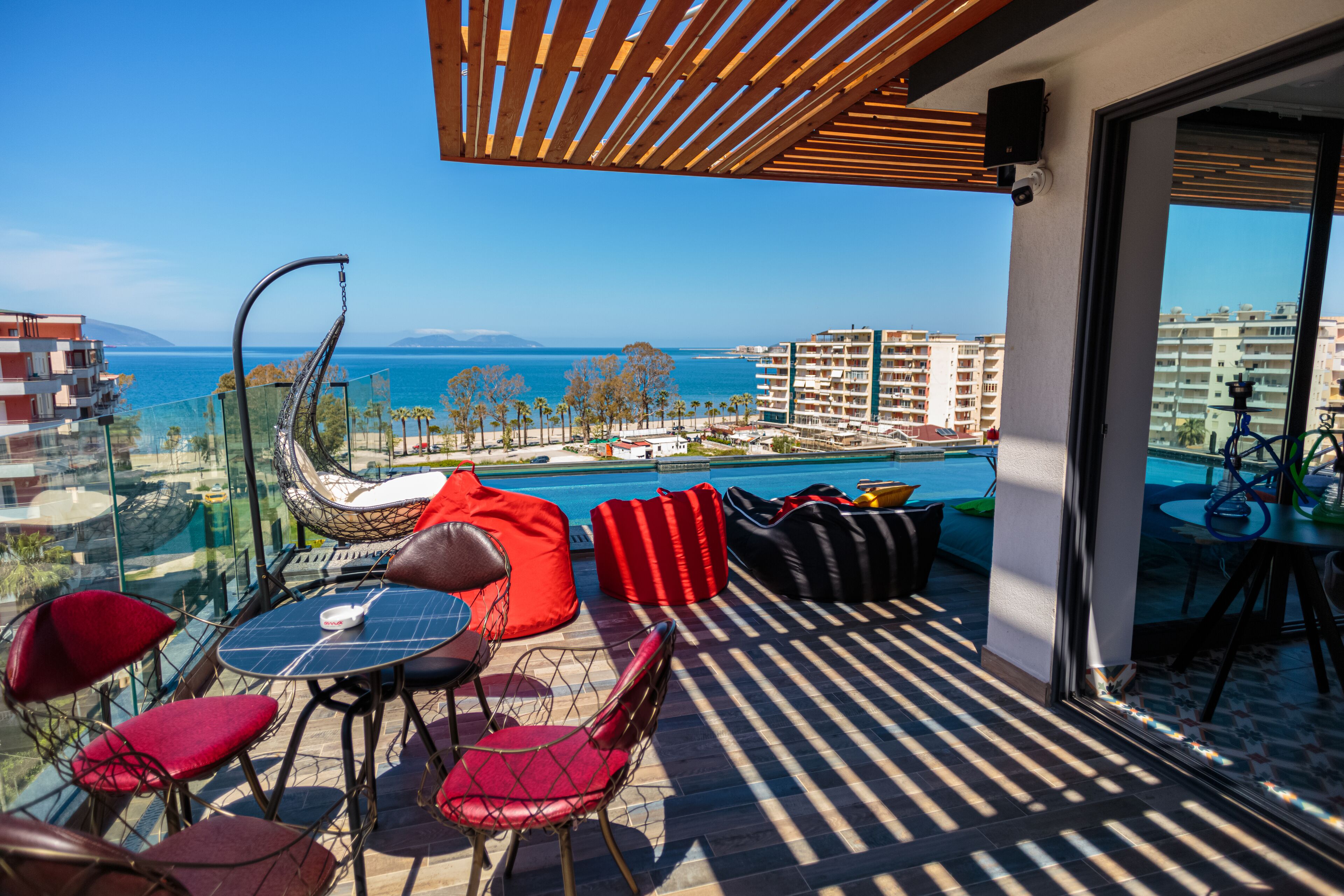 Un balcón con vista al mar, con mobiliario rojo y negro y una mesa con sillas.