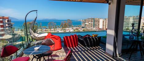 A balcony with a view of the sea, red and black seating, and a table with chairs.