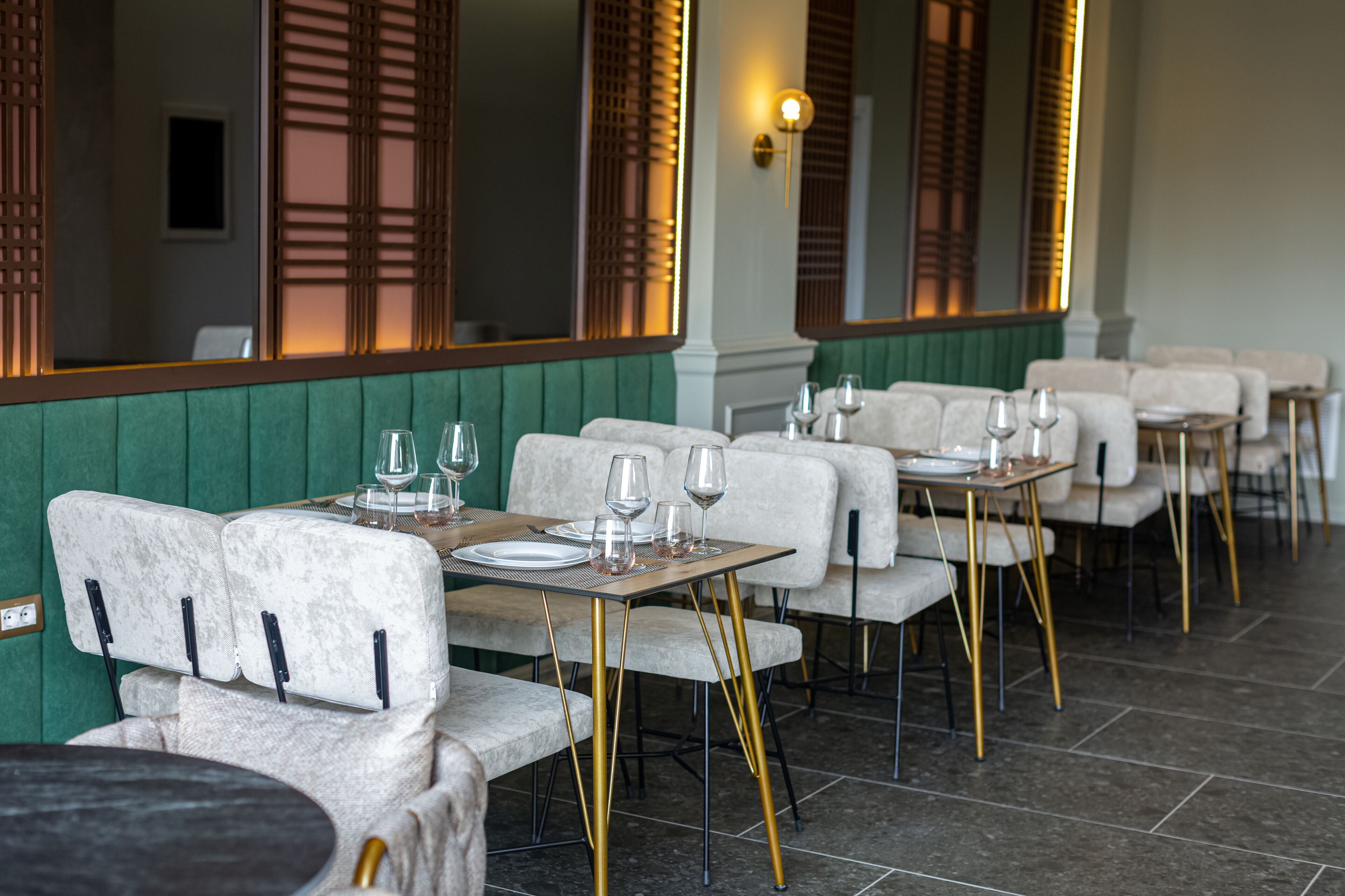 L’intérieur d’un restaurant présente des banquettes recouvertes d’un tissu vert, des chaises aux pieds dorés et un sol carrelé.