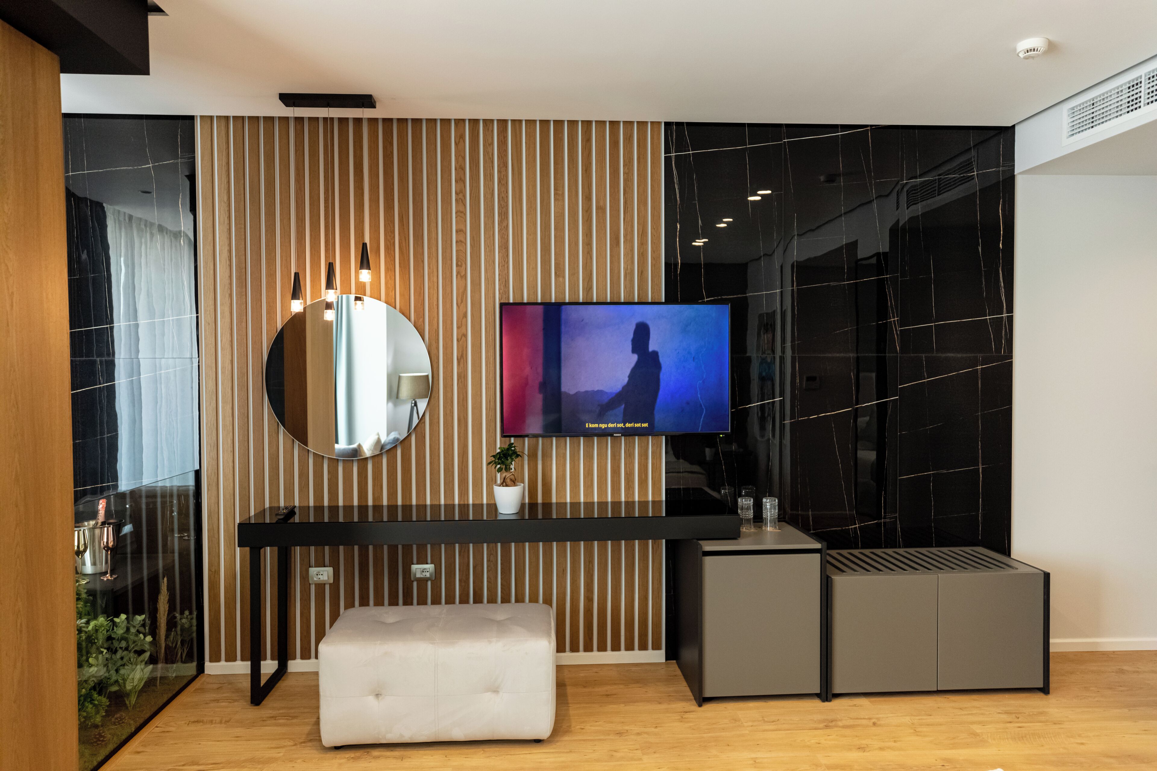 A modern living room with a TV, a round mirror, a small table, and a bench.