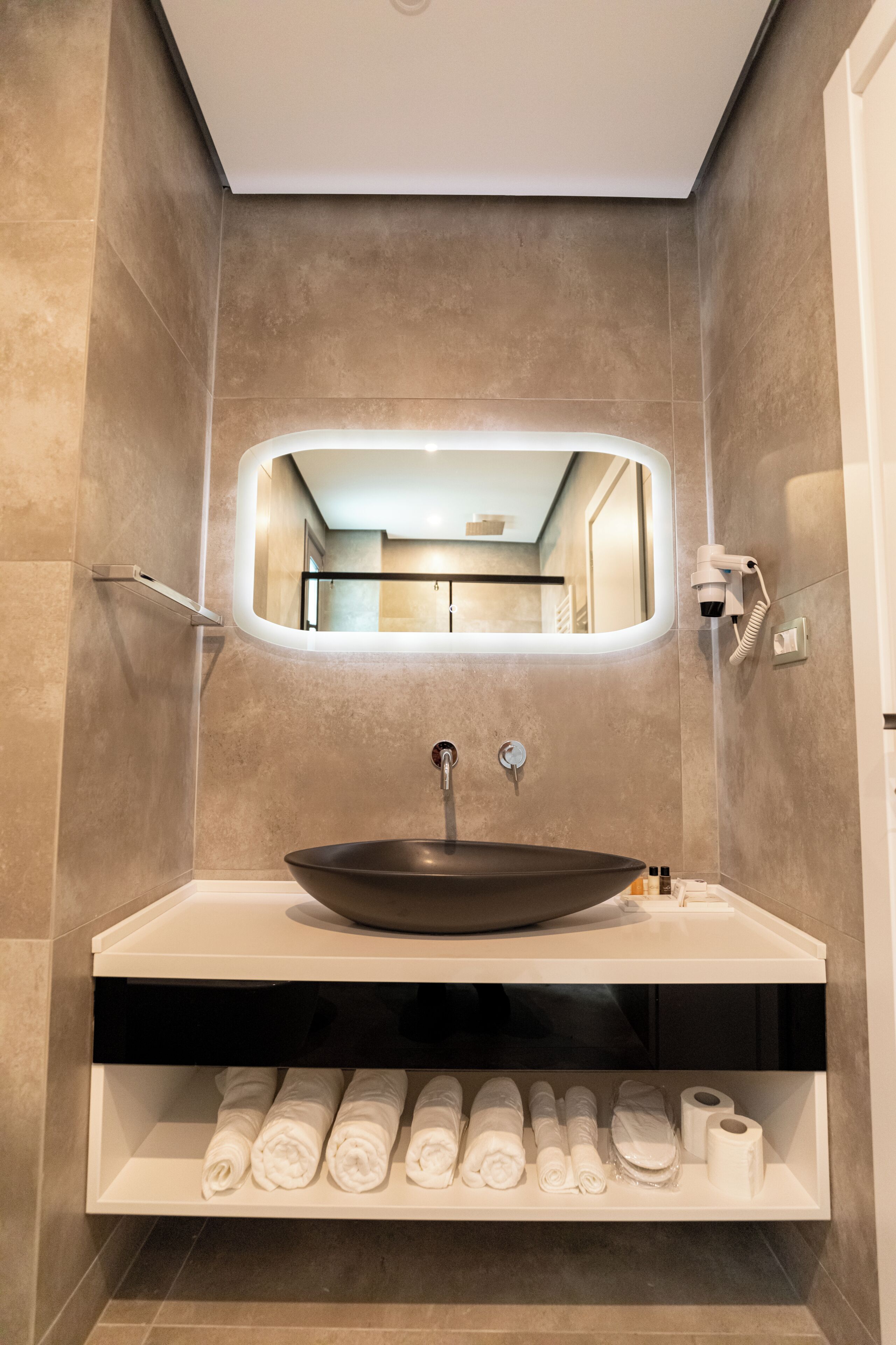 A modern bathroom with a large oval mirror, a vessel sink, and neatly rolled towels.