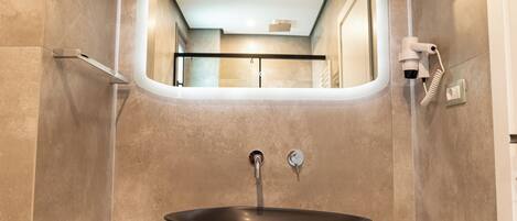 A modern bathroom with a large oval mirror, a vessel sink, and neatly rolled towels.