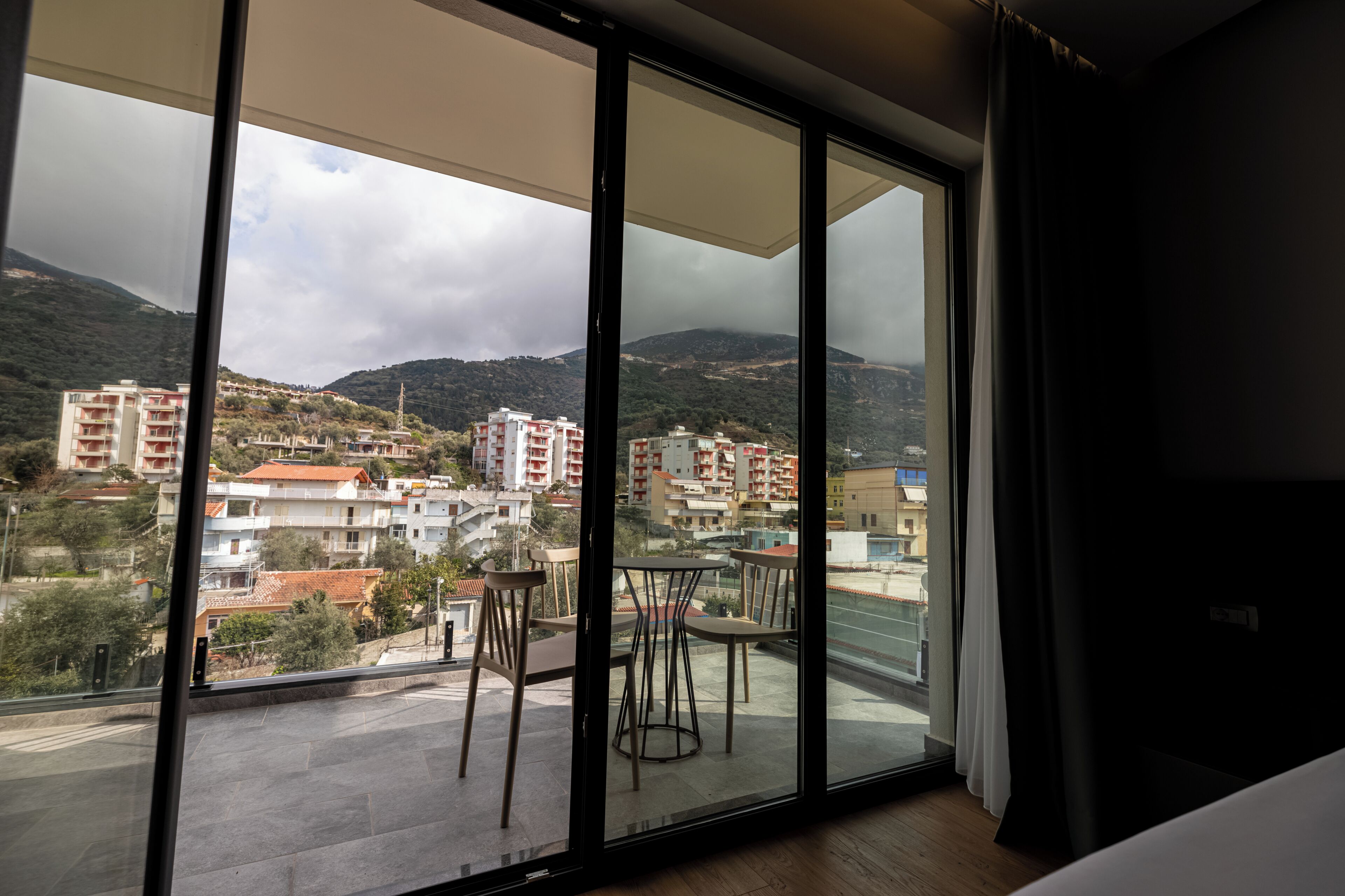 A balcony with a view of a hillside town, a table, and two chairs.