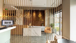 A hotel reception area with a marble counter, a reception desk, a seating area with a sofa and chairs, and a decorative wall with a geometric pattern.