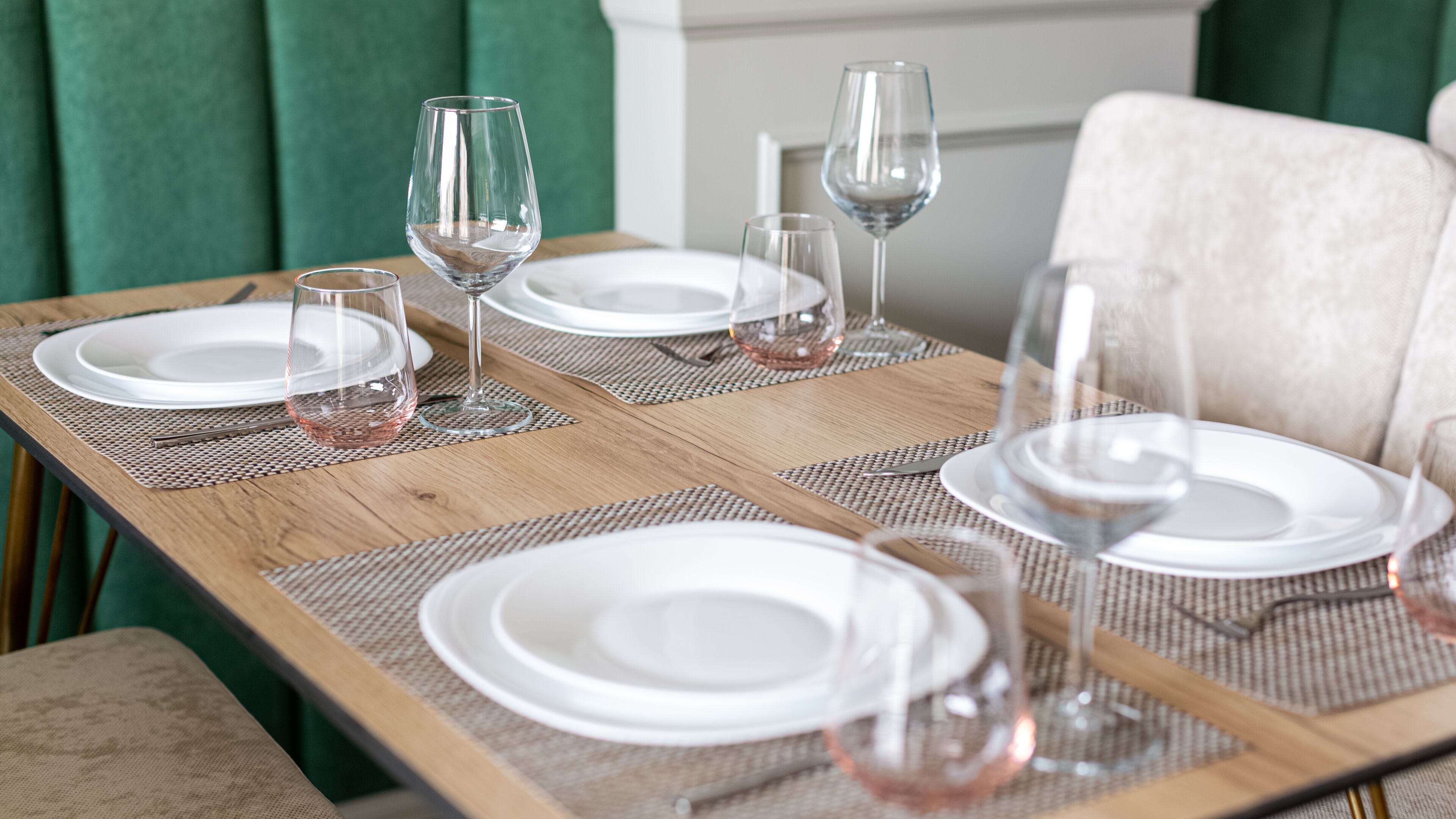 Une table à manger dressée avec de l’assiette blanche et des verres à vin, agrémentée d’un set de table en fibres tressées.
