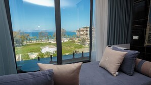A modern room with a large window, a sofa with cushions, and a view of a coastal area.