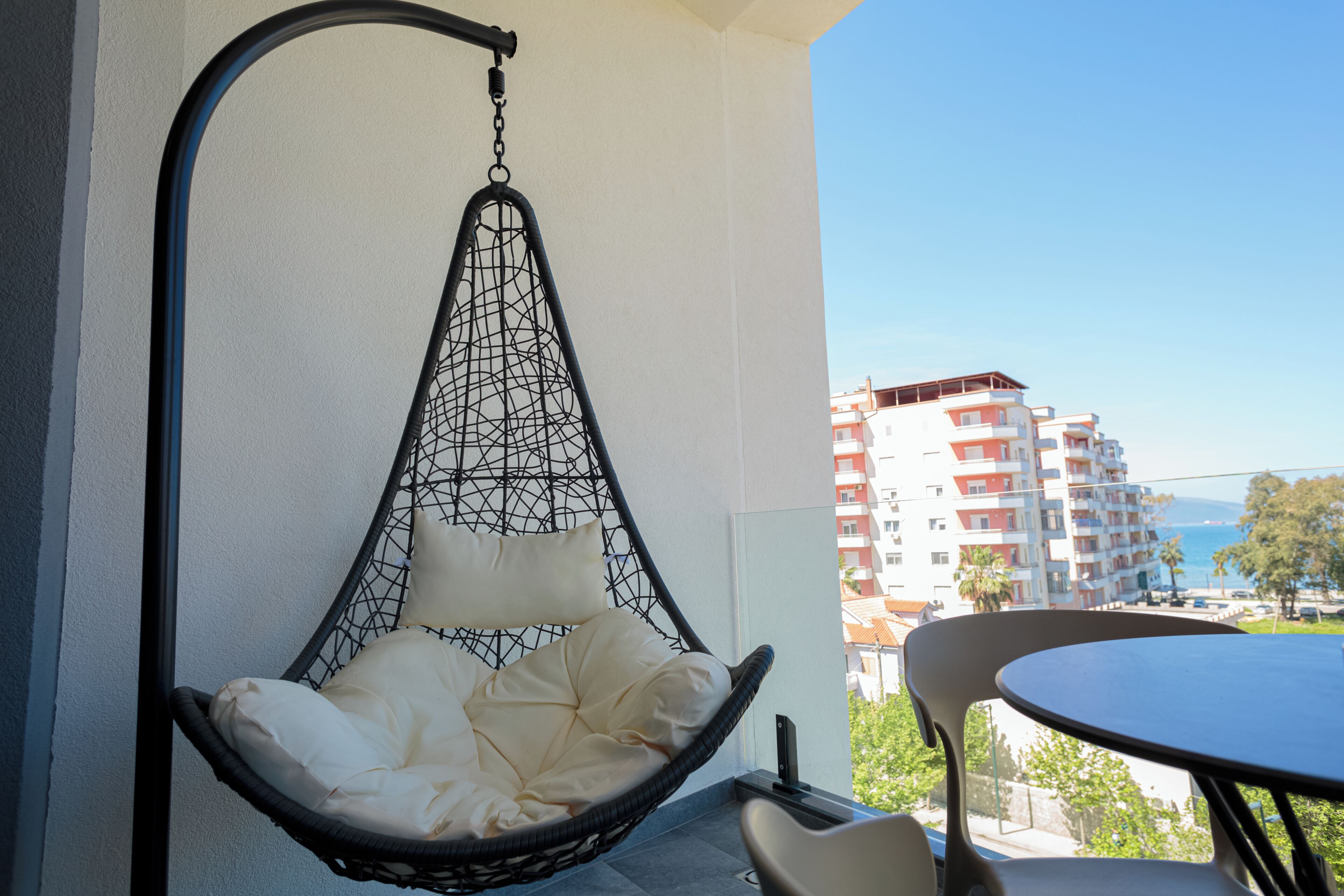 Un balcon avec un fauteuil suspendu, une table et une vue sur un immeuble à plusieurs étages.
