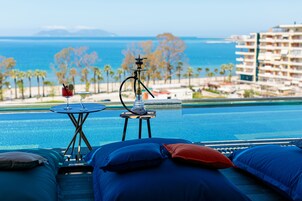 Un área de descanso junto a la piscina con vista al océano y palmeras.