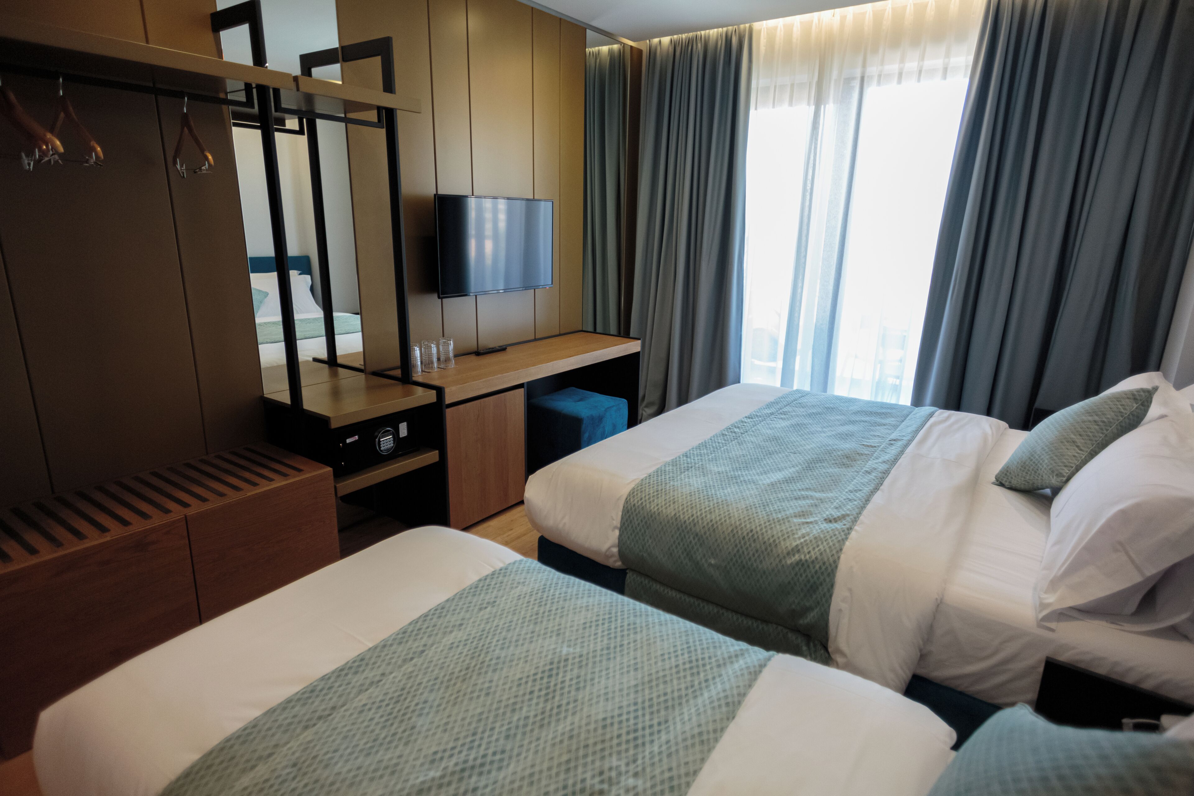 Ein Hotelzimmer mit zwei Betten, einem Fernseher, einem Schreibtisch und einem Kleiderschrank.