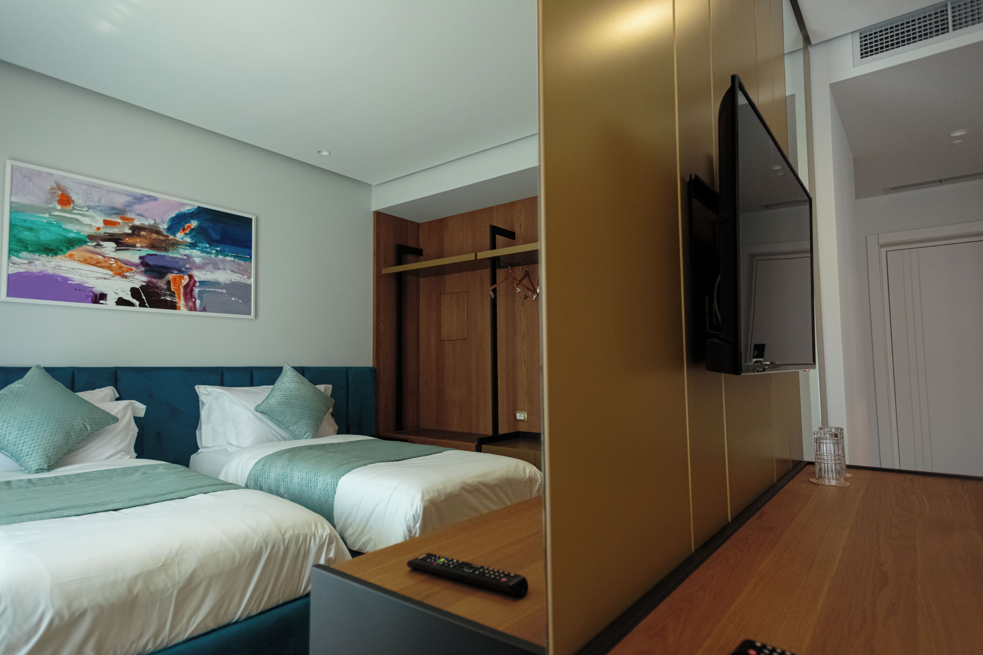 A hotel room with two beds, a TV, a wardrobe, and a painting on the wall.