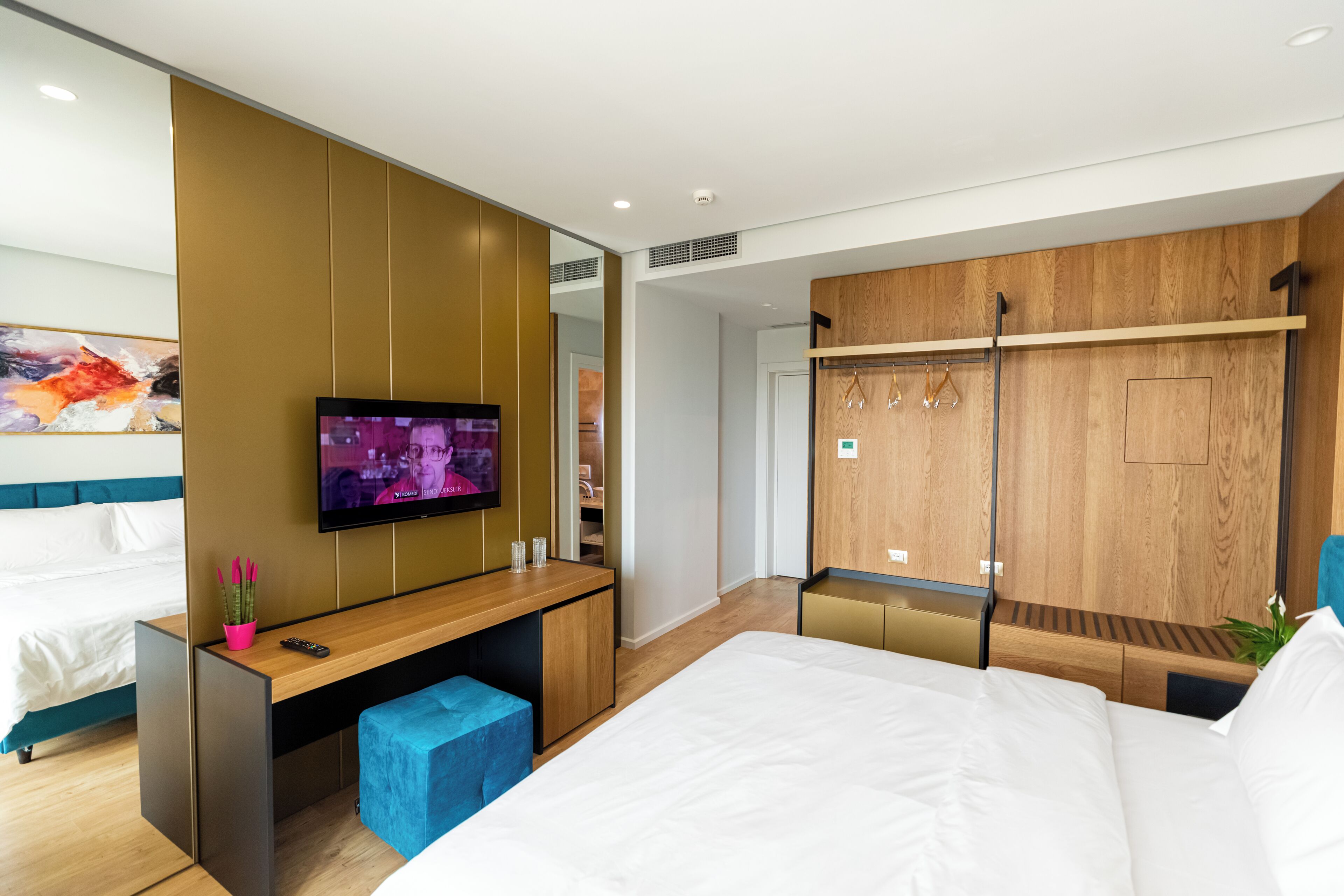 Een moderne hotelkamer met een bed, een aan de muur bevestigde televisie, een houten garderobe en een bureau met stoel.