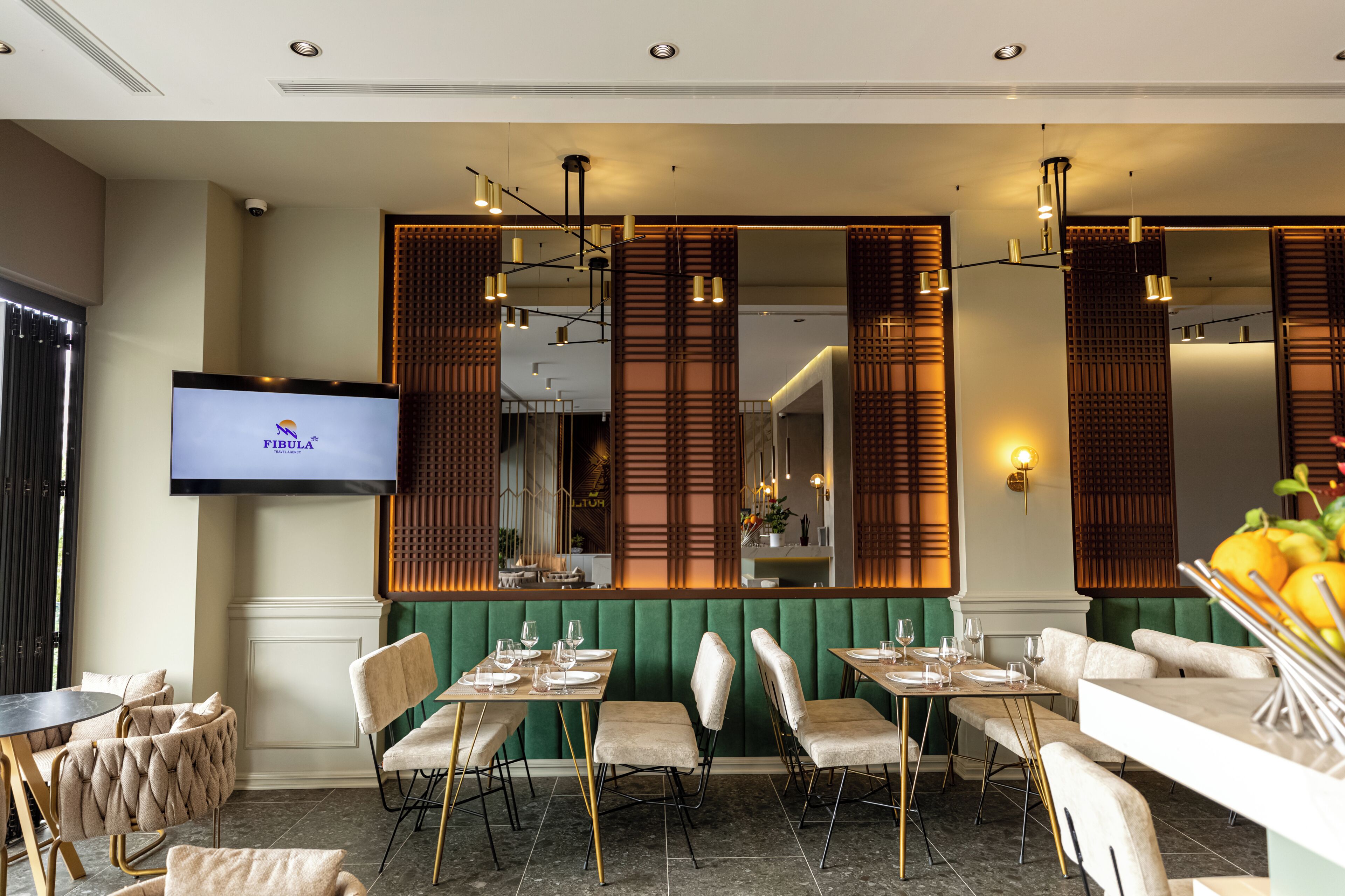 A restaurant with green upholstered booths, gold chairs, and a flat-screen TV on the wall.