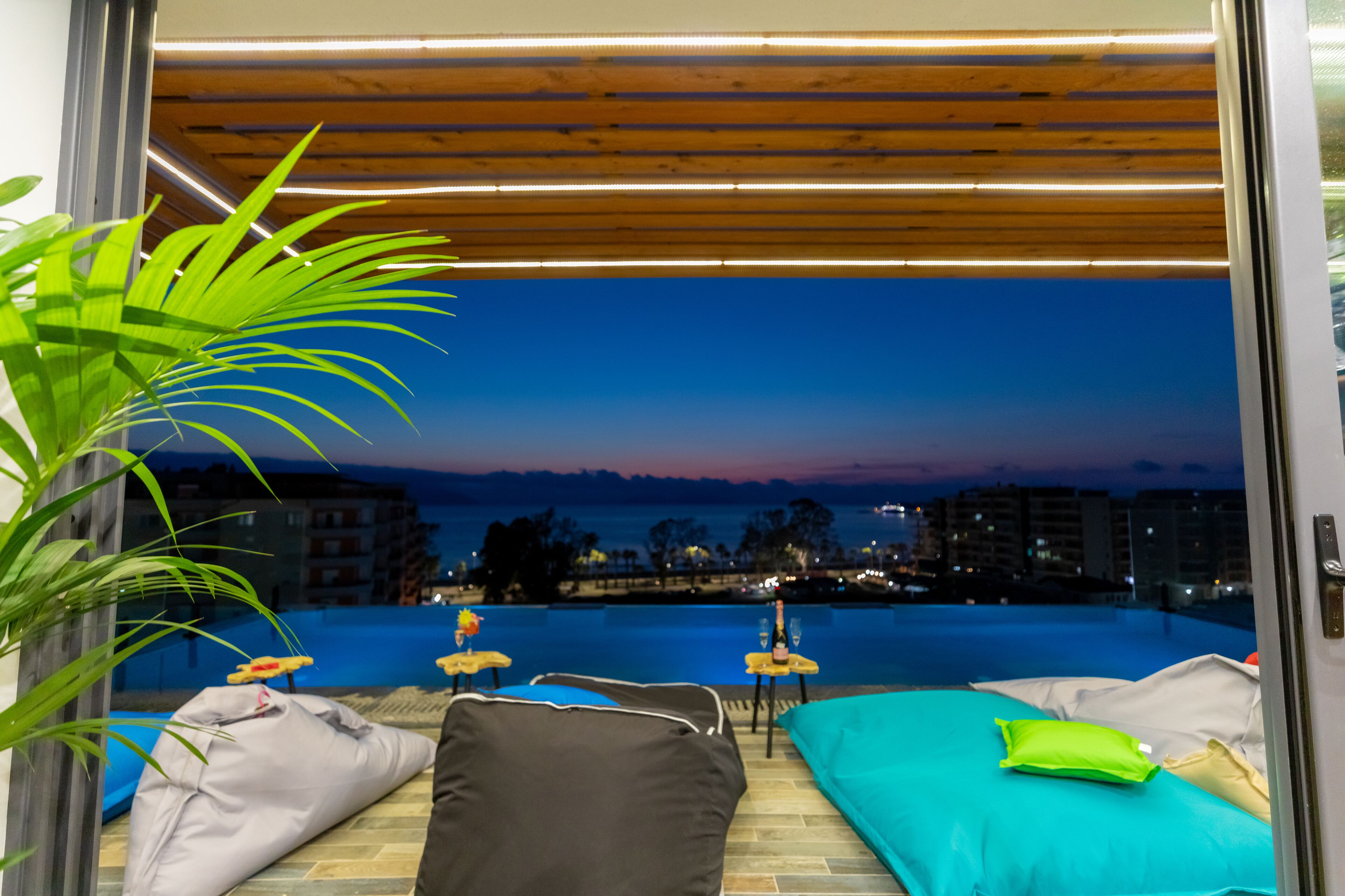 A modern room with a view of a swimming pool at dusk, a wooden ceiling, and a potted plant.