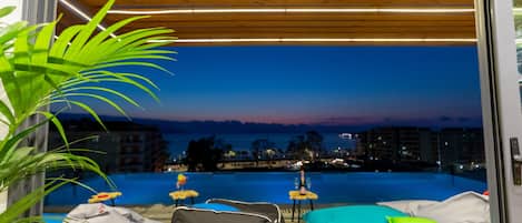 A modern room with a view of a swimming pool at dusk, a wooden ceiling, and a potted plant.