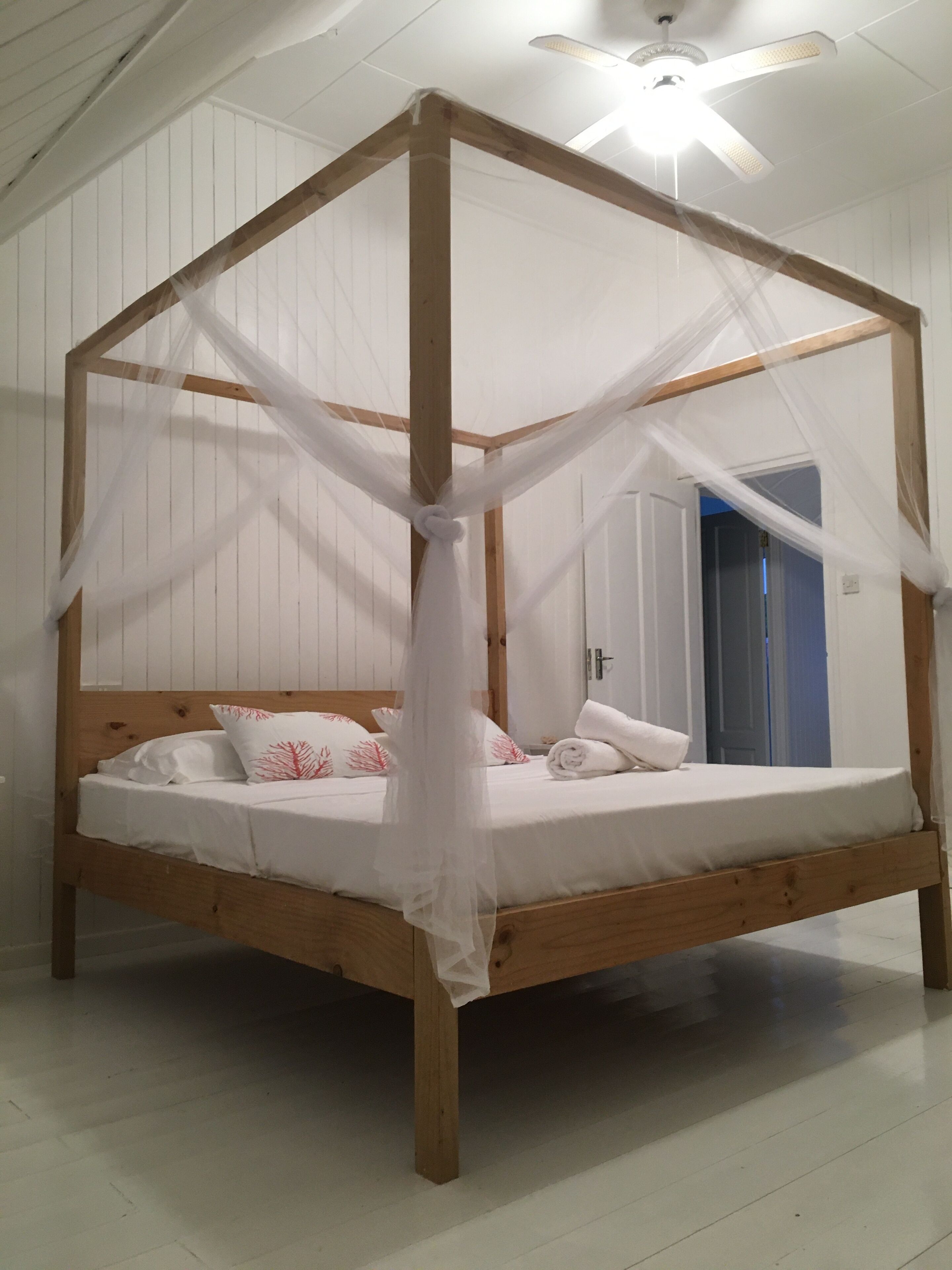 Una cama con dosel de madera, con dosel y ropa blanca, y almohadas decorativas.