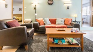 Una sala de estar con sofá, sillón, mesa de centro y un reloj de pared.