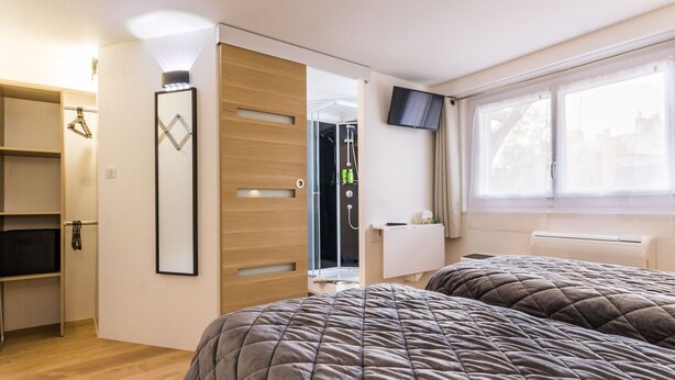 Un dormitorio con dos camas, un armario, zona de ducha y televisor en la pared.