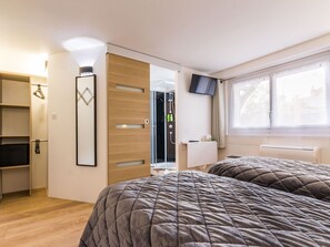 A bedroom with two beds, a wardrobe, a shower area, and a TV on the wall.