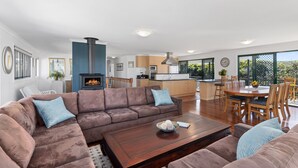 A spacious living room with a large brown sectional sofa, a wooden coffee table, and a fireplace. - Ideal Beach Family Getaway with Ocean Views (Noosa North Shore)