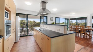 A modern kitchen with a central island, wooden cabinets, and a dining area with a table and chairs. - Ideal Beach Family Getaway with Ocean Views (Noosa North Shore)