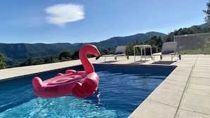 Ein Swimmingpool mit einem rosa Flamingo-Schwimmding, Liegestühlen und Blick auf Berge.