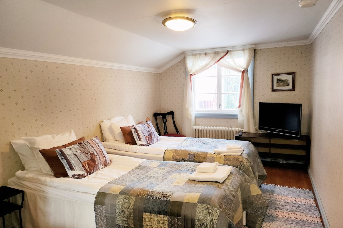 A hotel room with two beds, a television, and a window with curtains.